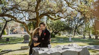 man holding woman by a grave as she cries holding a rose