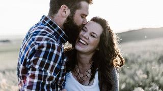 man kisses smiling woman on the cheek with eyes closed in a field