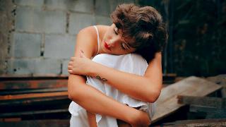 woman hugging in her knees with eyes closed sitting against brick wall