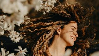 woman with curly hair flipping it surrounded by flowers