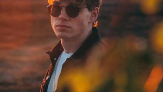 A man posing on a sunset-filled field with sunglasses on.