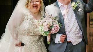 A man and woman with down syndrome leaving their wedding ceremony with smiles on their face.