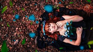 woman-in-black-dress-holding-bouquet-of-blue-flowers-while-lying-on-dried-leaves-