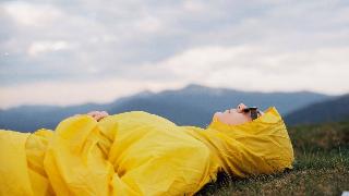 woman laying in yellow jacket on hill