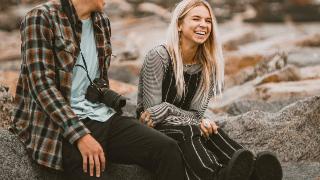 man-and-woman-sitting-on-a-rock laughing