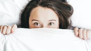 woman peeking from under the covers with green eyes