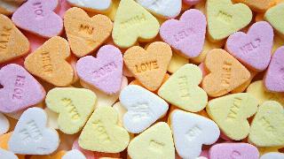 A number of bright candy hearts, one in the center has the word 'LOVE' stamped on it.