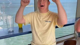 Dennis Peek in a yellow t-shirt on a boat, cheering.