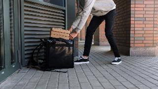 A man dropping off a food delivery in front of someone's door. 