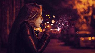 woman blowing into sparkles on sidewalk in her hand