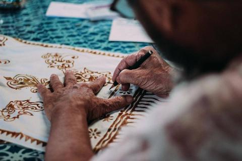 A man hand-painting floral details on a white garment.