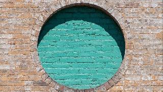 A brown brick wall with a circle of teal-painted bricks.