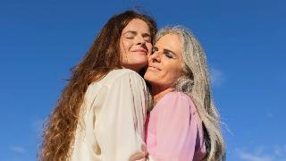 Two women hugging in front of a blue sky.