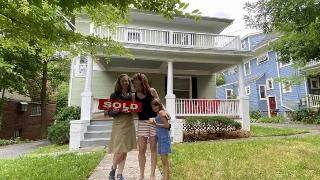 Two of the women and one kid standing in front of the house with the 'sold' sign.