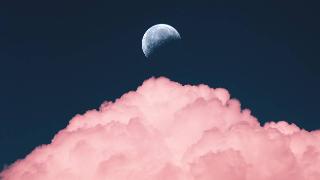 The moon in the sky above a large, pink lit cloud.