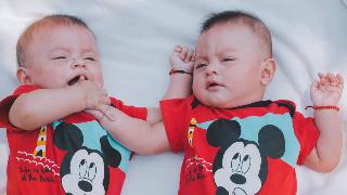 Two twin babies laying on a blanket.