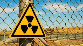 A triangular radiation sign on top of a chain link fence.