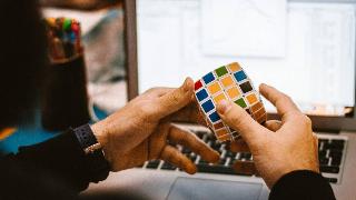 Someone solving a rubiks cube puzzle in front of their computer.