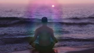 A man sitting on a beach with a colorful aura glowing around him.