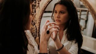 A woman looking in a mirror, oval with a gold frame.