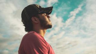 man in red shirt tipping head back to sun in sky