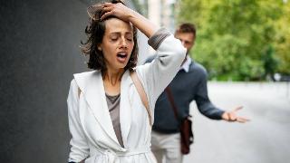 A couple fighting outside, the woman looking distressed and walking away while the man follows her.