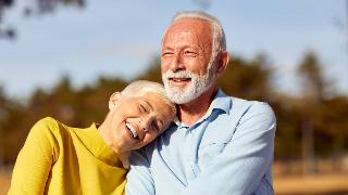 A happy couple, the woman leaning her head against her husband's shoulder, both smiling in the sunshine.