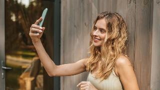 A young woman taking a selfie as she leans against a wooden wall.