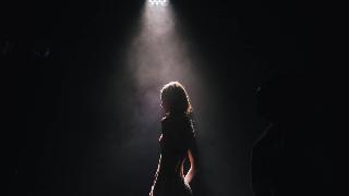 A woman on a dark stage lit only by a spotlight.