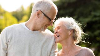 A couple smiling at one another outside, the woman leaning on the man's shoulder.