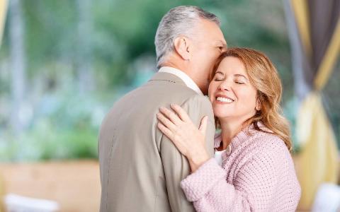 A couple hugging while standing outside, seen from over the man's shoulder toward the woman.