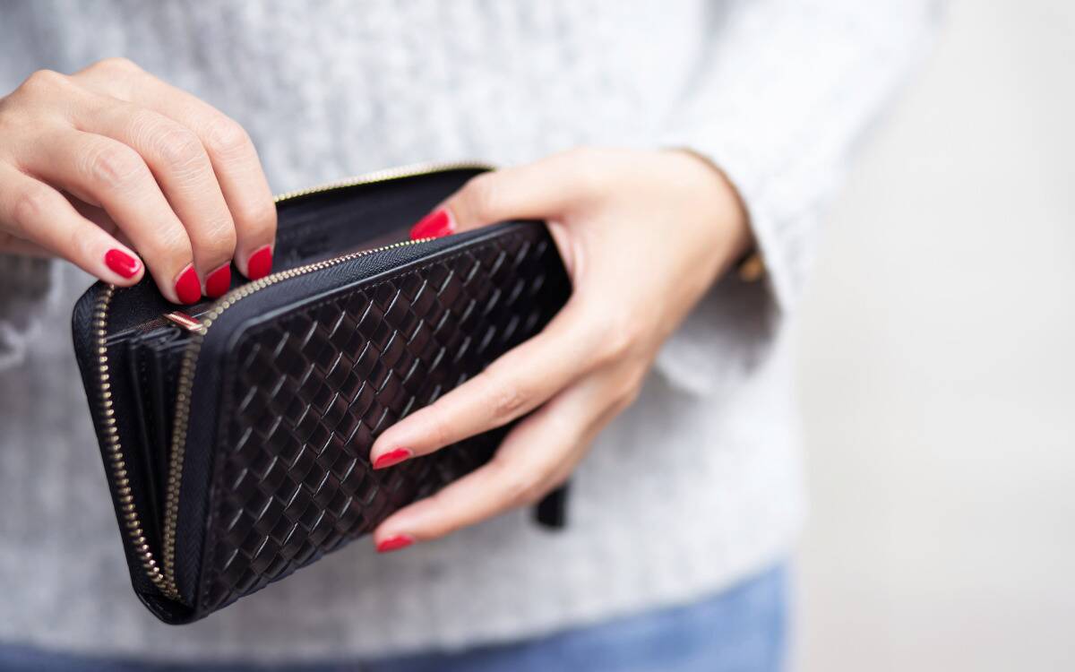 A woman with red nails reaching into her black zip-up wallet.