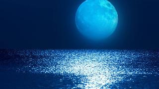 A large blue moon rising above a shimmering body of water.