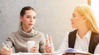 Two women talking as they work, one looking concerned.