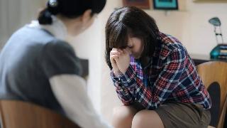 A girl leaned over, forehead in her hands, looking distressed as she speaks to a therapist.