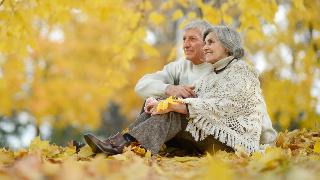 A couple sitting next to one another in the autumn fallen leaves.