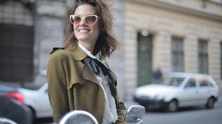 A stylish woman standing on a city street, smiling confidently.