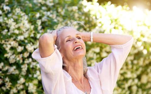 A woman looking carefree outside, hands up in her hair, head leaned back as she laughs.