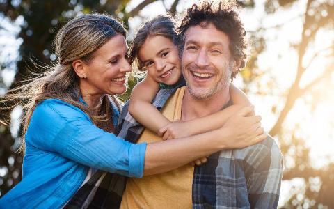 A couple and their young daughter all hugging and smiling together.