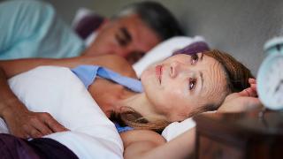 A woman awake in bed while her husband sleeps next to her.