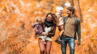 A family of four, a couple and two young daughters, walking down an autumn path.