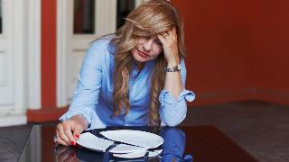 A woman sat at a table in front of a broken plate, looking disraught.