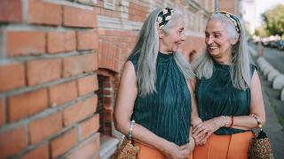 Two older women standing next to each other in matching outfits, smiling.