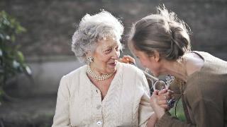 An older woman speaking to and smiling with a younger woman, the two are holding hands.