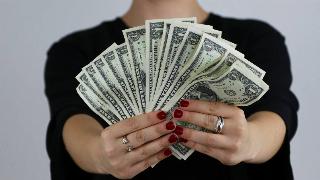 A woman holding a fan of $1 bills out in front of her.