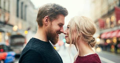 A couple standing nose-to-nose, smiling, in the middle of a street.