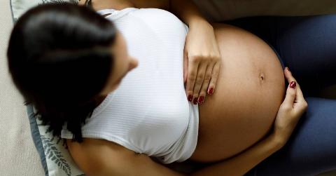 A woman laying on her couch, holding her pregnant stomach.