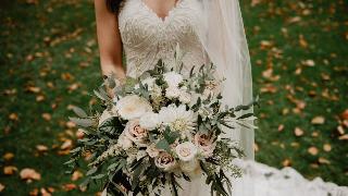 A bride holding a large bouquet in front of her dress.