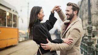 A couple smiling and dancing out on the street.