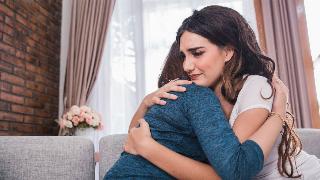 Two friends hugging, the one whose face we can see appearing sad.